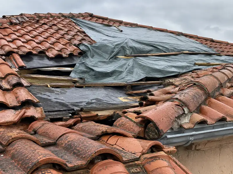 Toiture en tuiles cassées recouverte d'une bâche de protection après infiltration